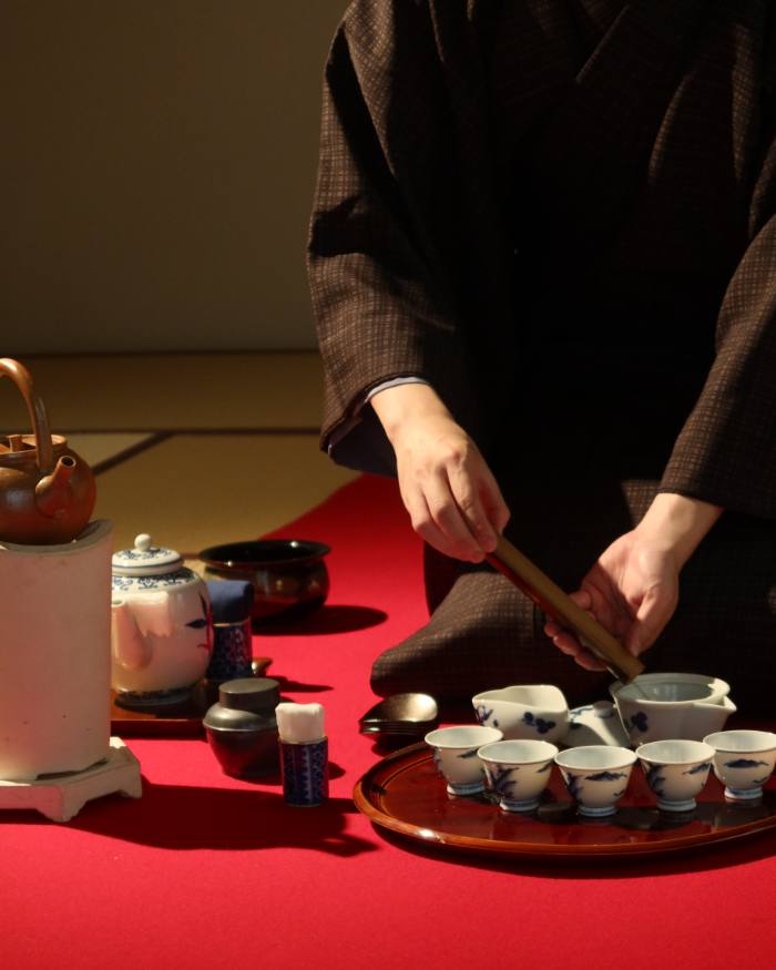 Hands setting out teacups on a red cloth for a tea gathering