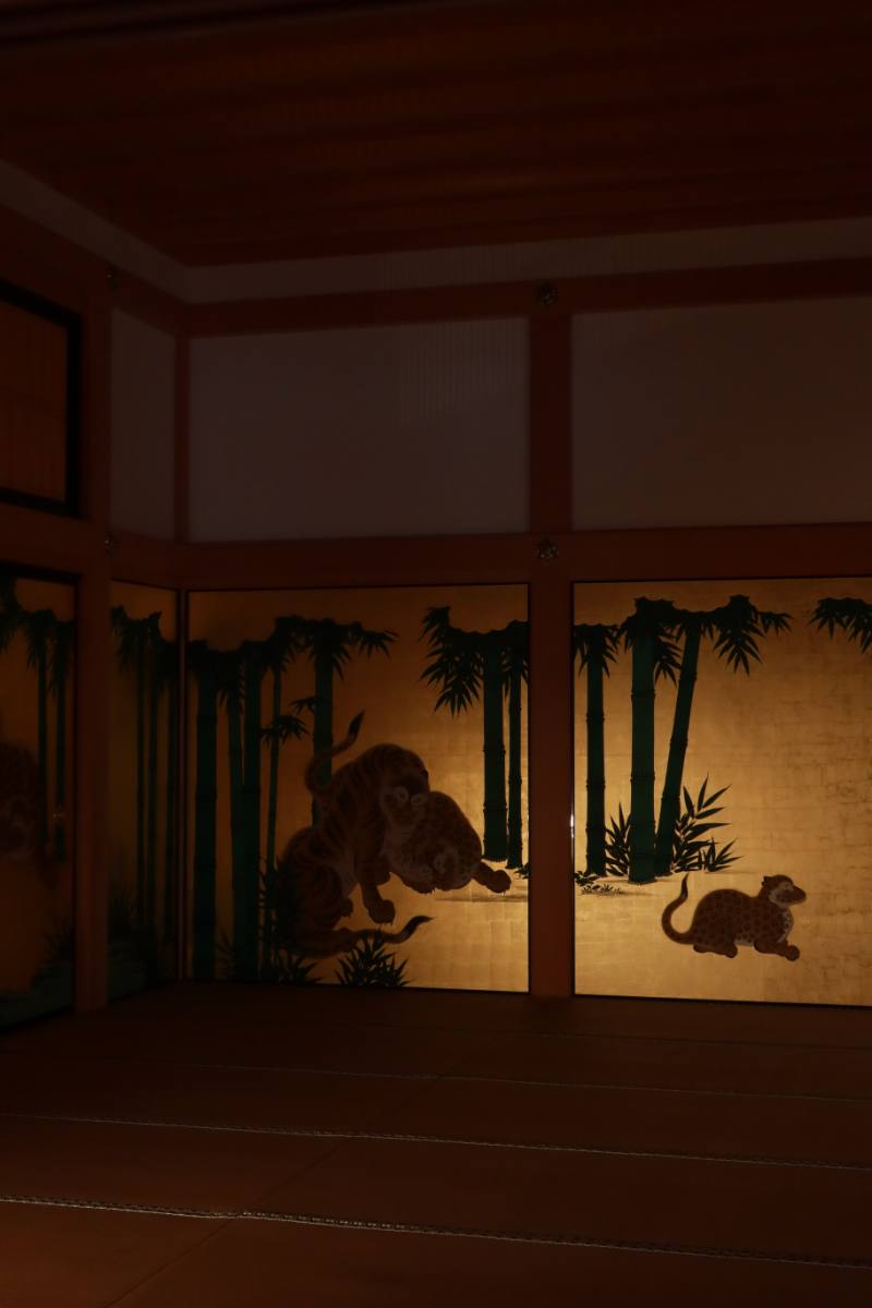 A softly lit Japanese room with gold panels depicting tigers and bamboo