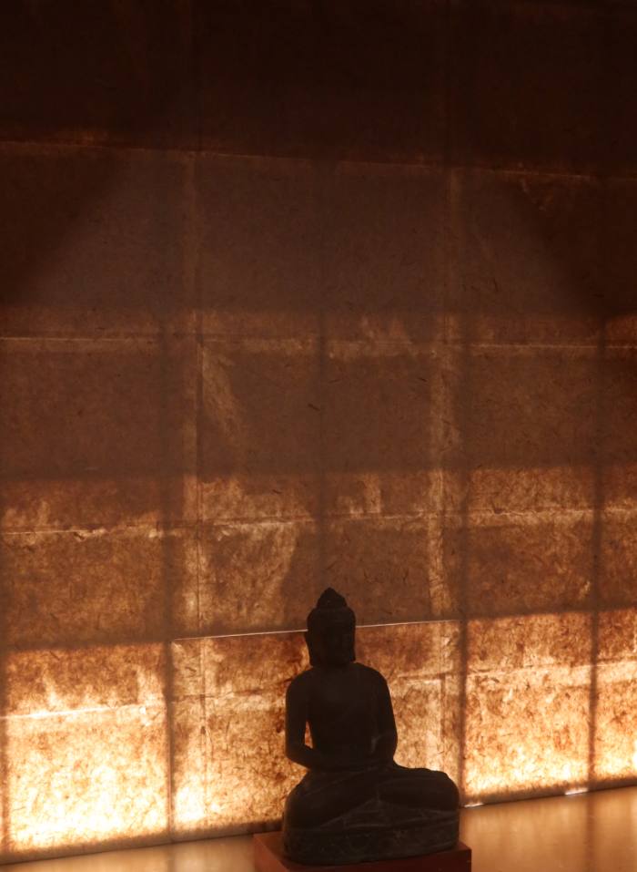 A small Buddha figure silhouetted against a glowing paper wall